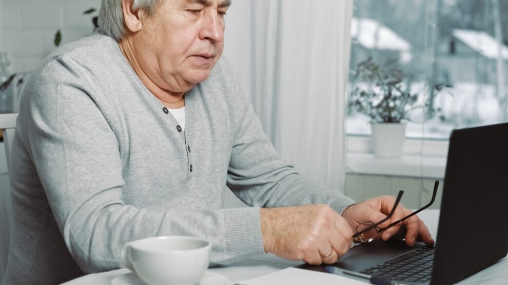 Une personne âgée examine avec méfiance un e-mail suspect sur son ordinateur portable.